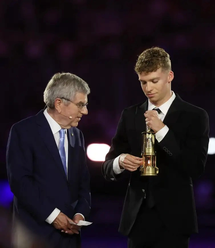 O medalhista francês Leon Marchand com a chama olímpica ao lado de Thomas Bach, presidente do Comitê Olímpico Internacional (COI)