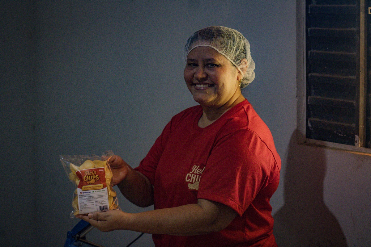 Dona Socorro segura um pacote lacrado dos chips de macaxeira, pronta para a venda