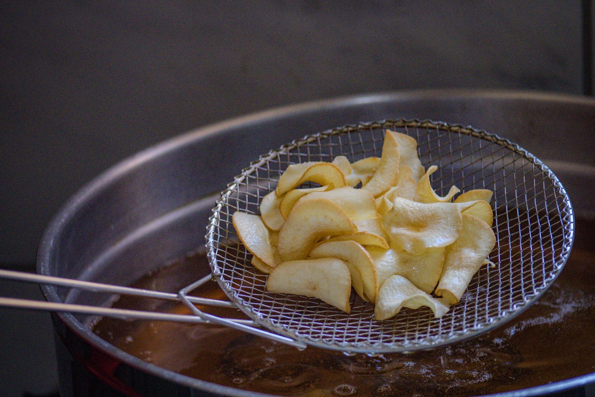 Dona Socorro verifica cuidadosamente o ponto dos chips durante a fritura