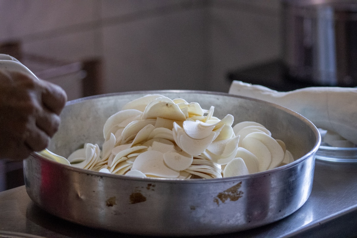 Macaxeiras recém-fatiadas são dispostas na forma, prontas para a fritura